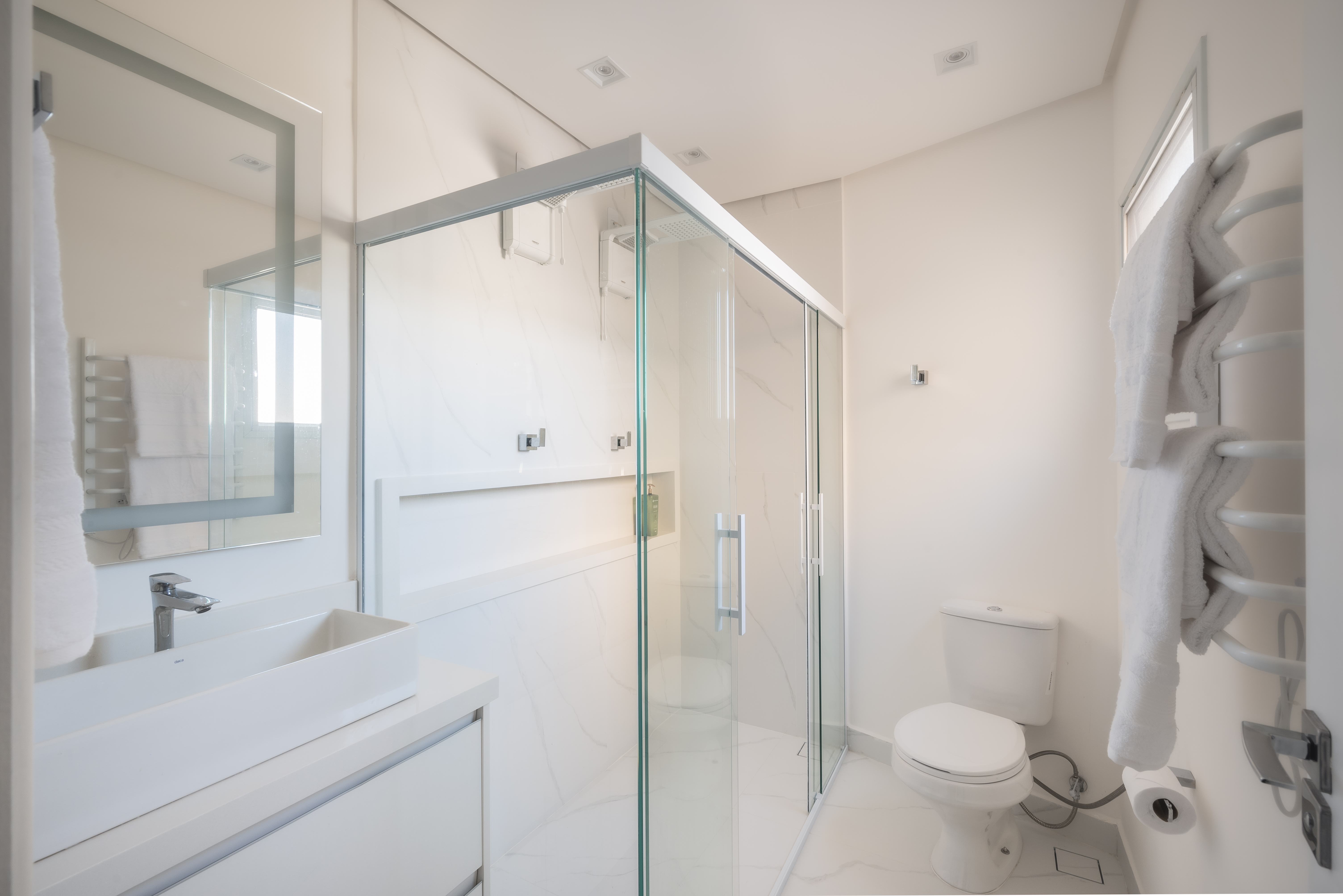Projeto de PB Arquitetura. Na foto, banheiro branco com armário branco e box de vidro.