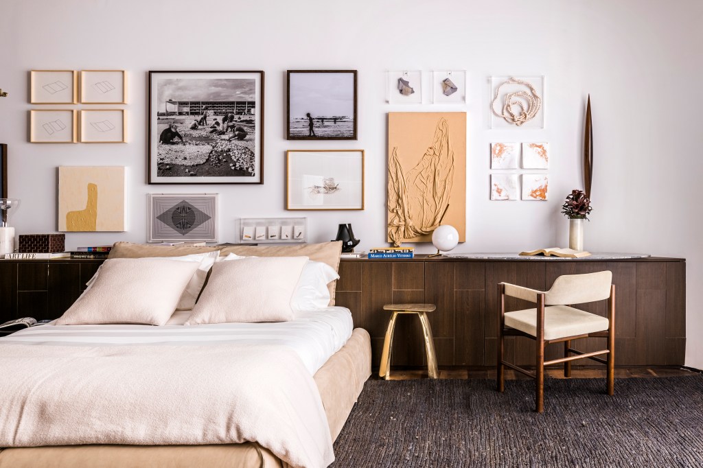 Quarto com cama de casal e bancada de madeira escura com cadeira; quadros na parede.