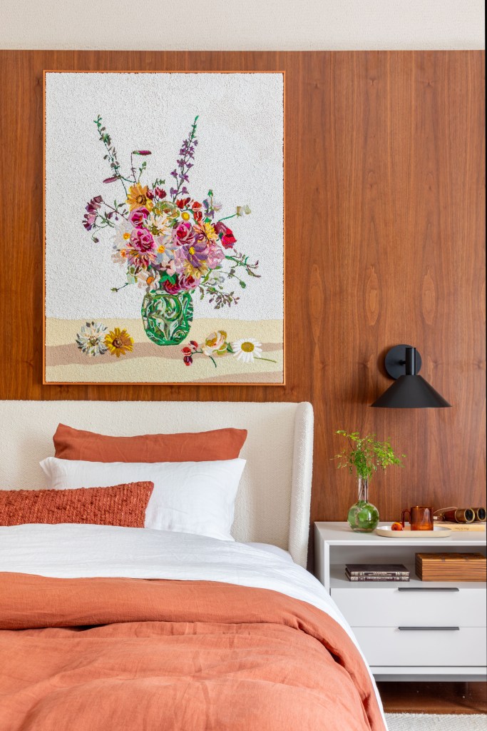 Suíte ganha conforto quarto de hotel com paredes de madeira. Projeto de Paula Muller para a CASACOR Rio 2023. Na foto, quarto com paredes de madeira e quadros.
