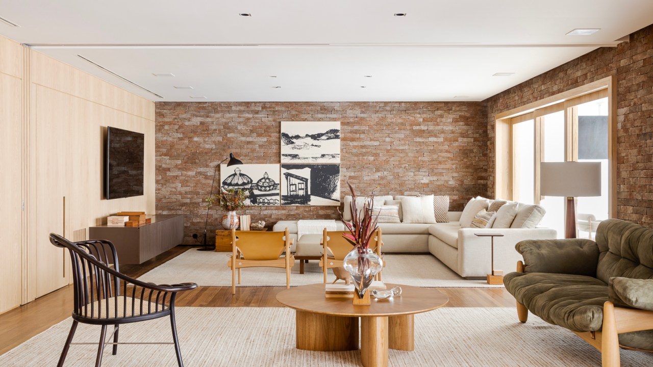 Tijolinhos revestem todas as paredes do living deste apê de 310 m². Projeto de Très Arquitetura. Na foto, sala com sofá em L, quadros e poltronas.