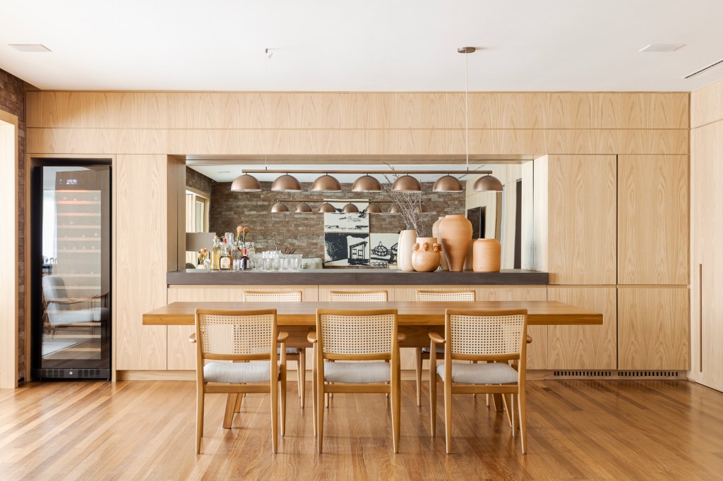 Tijolinhos revestem todas as paredes do living deste apê de 310 m². Projeto de Très Arquitetura. Na foto, sala de jantar com cadeira de palhinha, espelho e bar.