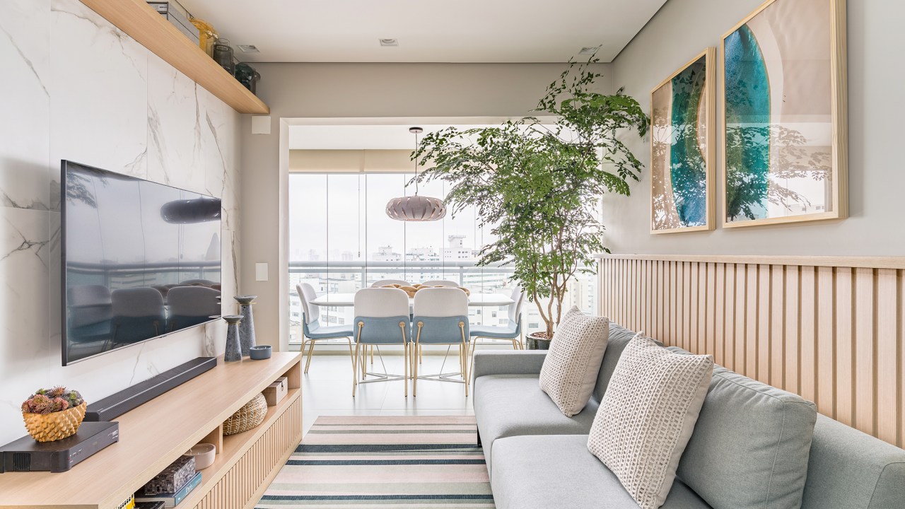 Apartamento de 60 m² ganha décor delicado repleto de madeira e plantas. Projeto de Bia Hajnal. Na foto, sala de estar com sofá cinza, lambri e tapete listrado.