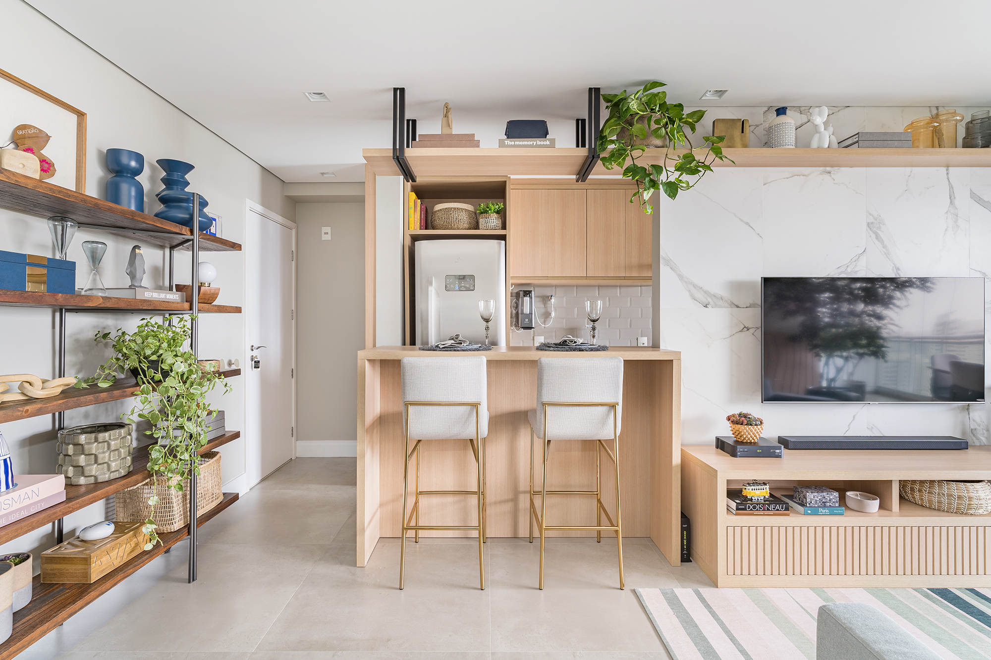 Apartamento de 60 m² ganha décor delicado repleto de madeira e plantas. Projeto de Bia Hajnal. Na foto, cozinha americana com balcão, prateleira suspensa e estante com lembranças de viagem.