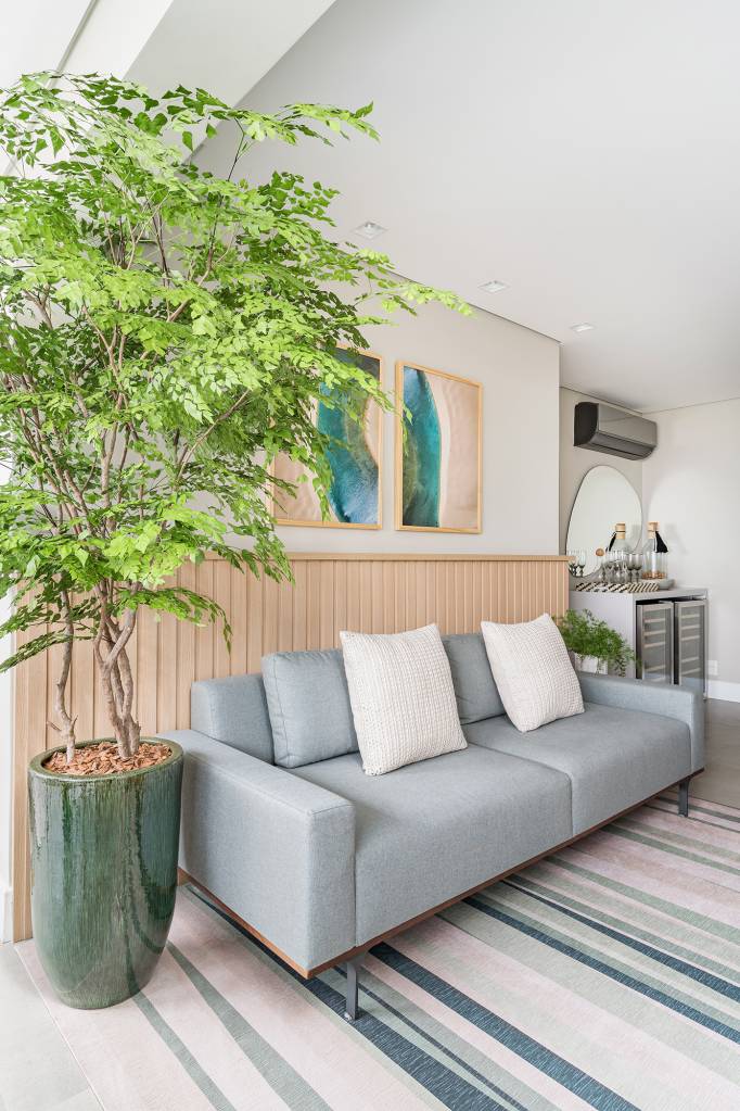 Apartamento de 60 m² ganha décor delicado repleto de madeira e plantas. Projeto de Bia Hajnal. Na foto, sala de estar com sofá cinza e lambri de madeira., Arvore em vaso.