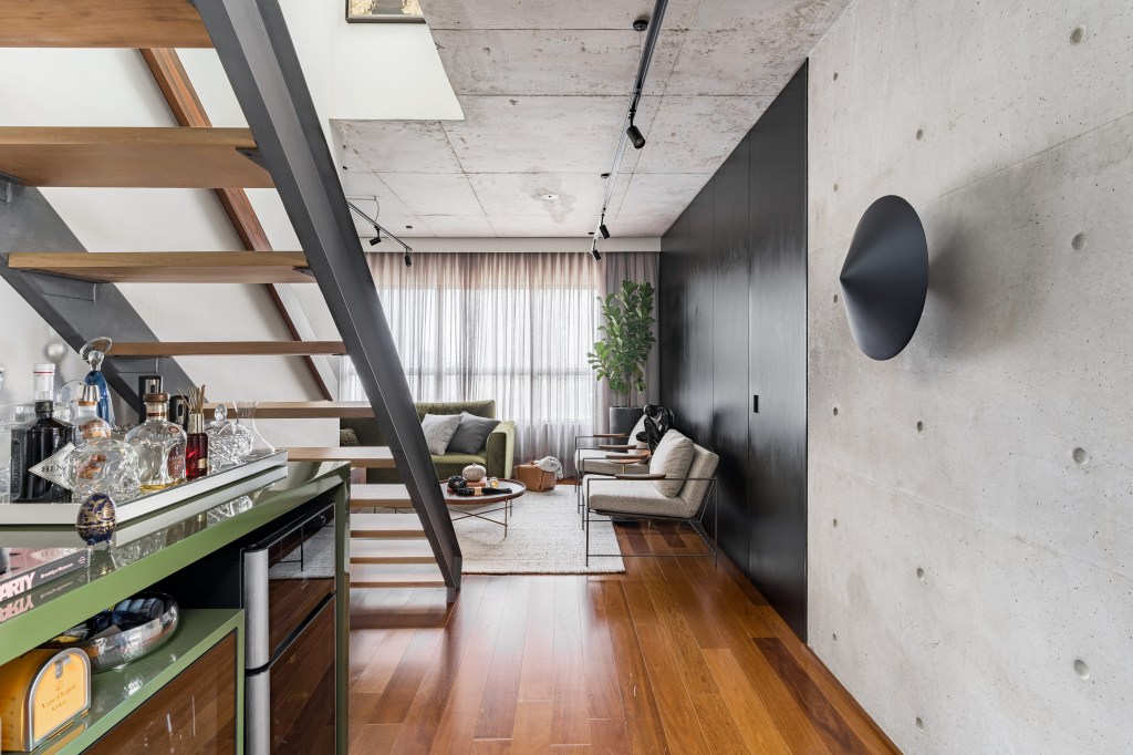 Apê de 140 m² com estilo industrial tem pia no quarto e jardim de cactos. Projeto de Gabriela Prado. Na foto, sala com escada, bar e paredes pretas.