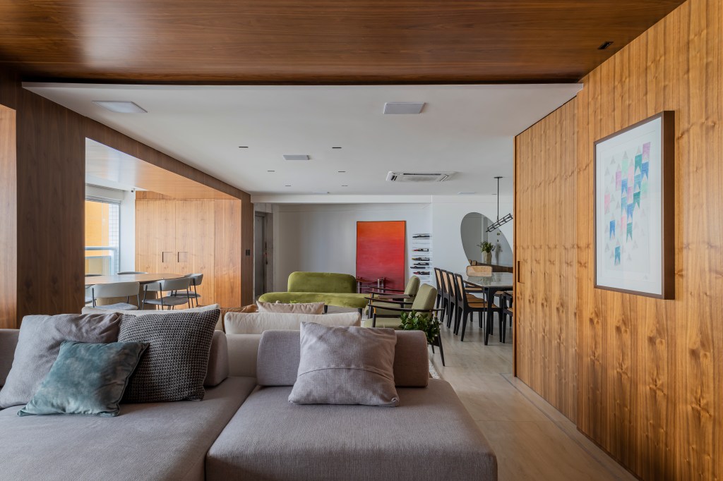 Projeto de Romário Rodrigues. Na foto, sala de estar integrada com paredes revestidas de madeira, sofá cinza, sofá verde curso, poltronas verdes.