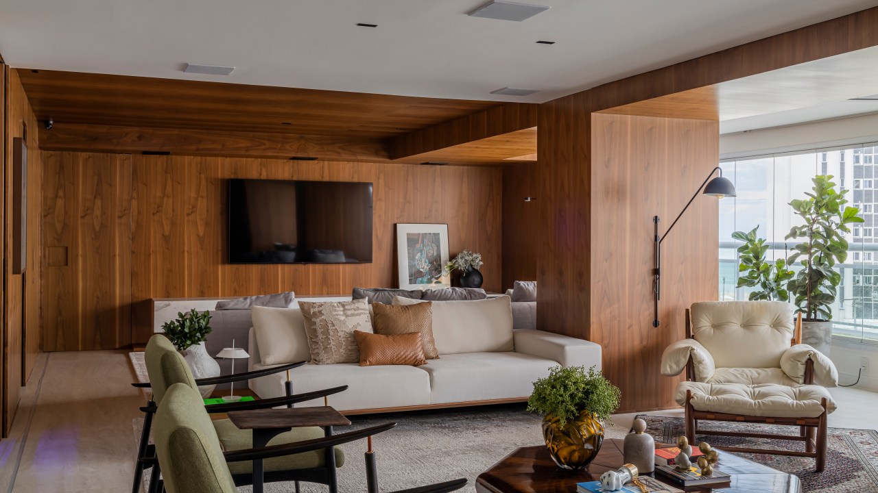 Projeto de Romário Rodrigues. Na foto, sala de estar revestida de madeira com sofá claro, poltronas verdes e mesa de centro.