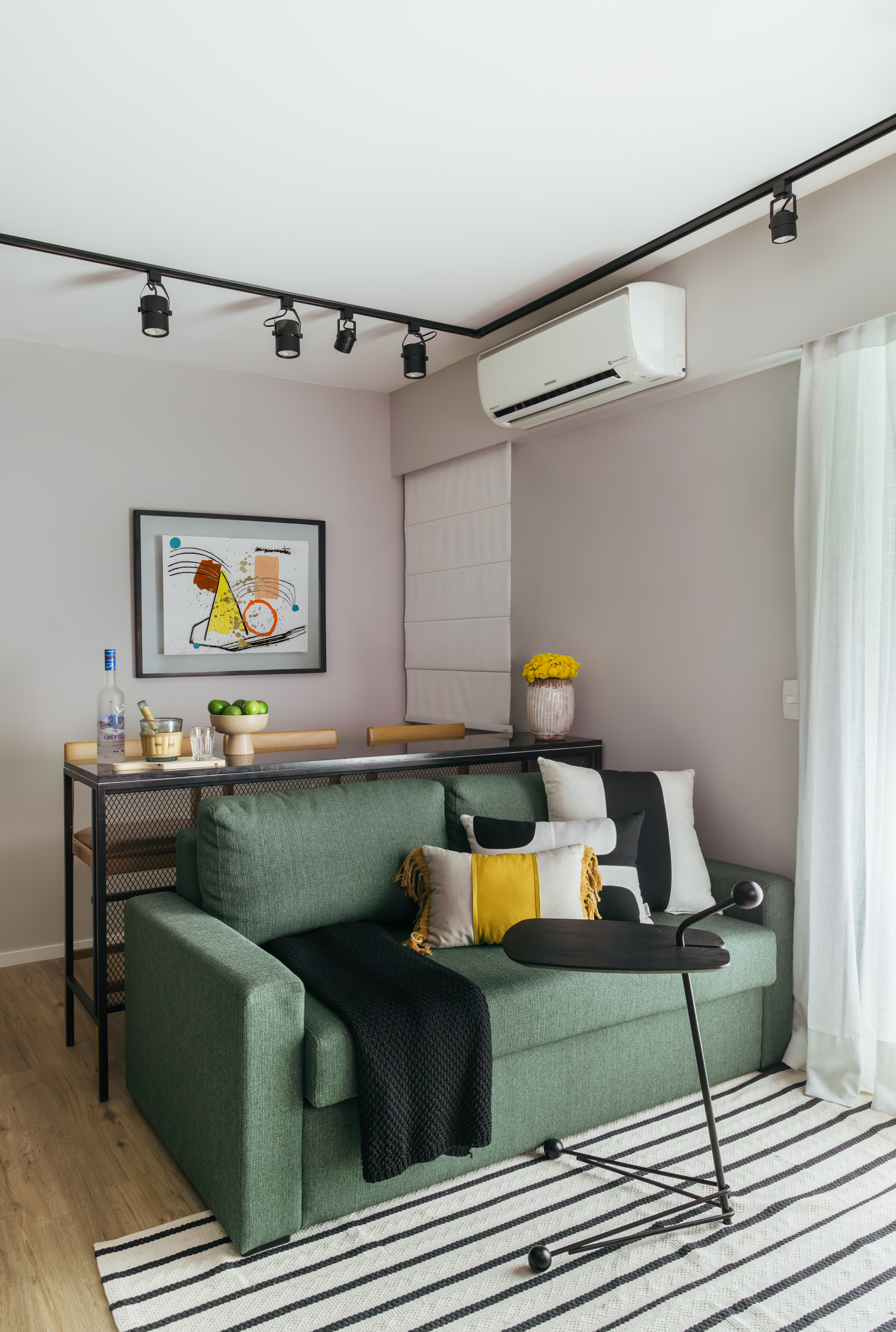 Projeto de Ikeda Arquitetura. Na foto, sala de estar pequena com trilhos de spots e sofá verde.