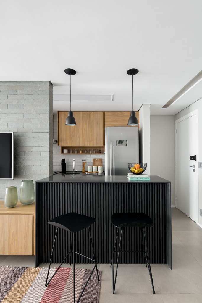 Projeto de Studio Dyo. Na foto, cozinha integrada com bancada ripada preta e banquetas pretas.