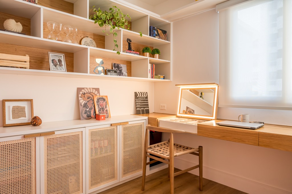 Projeto de Paula Scholte. Na foto, home office com estante de marcenaria com nichos, bancada de madeira e penteadeira retrátil.