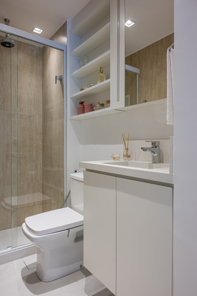 Projeto de Paula Scholte. Na foto, banheiro pequeno com revestimentos e marcenaria branca e armário aéreo.