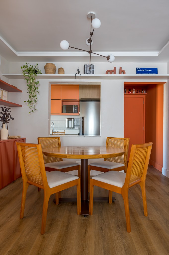 Projeto de Paula Scholte. Na foto, sala de jantar com buffet laranja, mesa de madeira redonda com quatro cadeiras. Cozinha ao fundo com paredes laranjas.