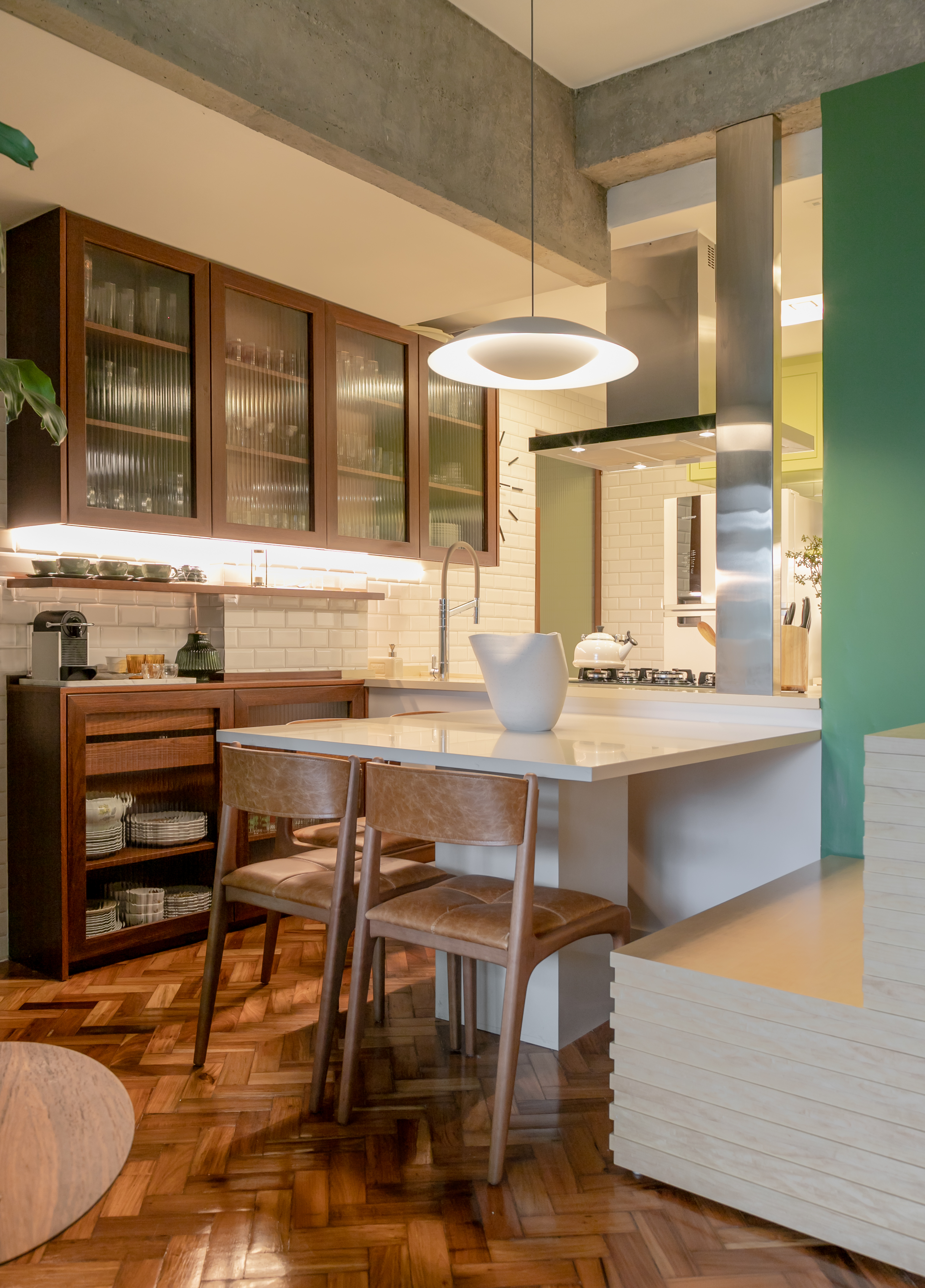 Projeto de Marcela Martins. Na foto, cozinha com cristaleira de vidro canelado, marcenaria verde, ilha e piso de taco.