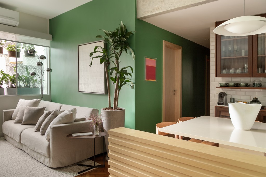 Projeto de Marcela Martins. Na foto, sala integrada com cozinha e parede verde.