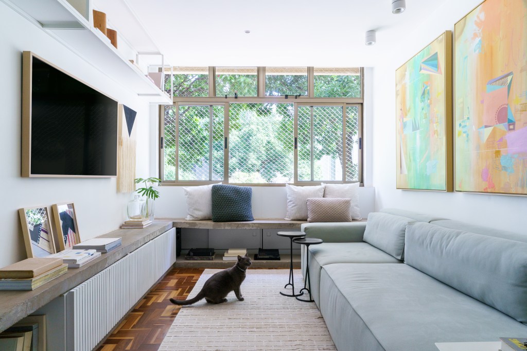 Projeto de Traama Arquitetura. Na foto, sala de estar com piso de taco, sofá cinza azulado claro e banco de concreto.