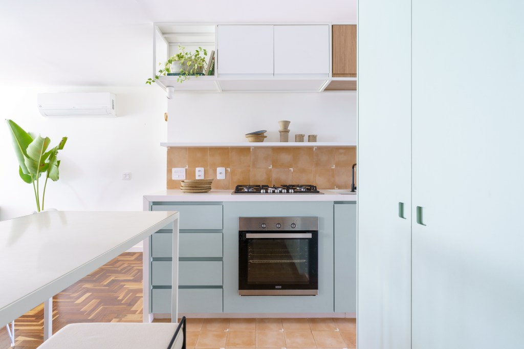 Projeto de Traama Arquitetura. Na foto, Cozinha integrada clara com piso de ladrilho hidráulico, marcenaria azul e bancadas brancas.