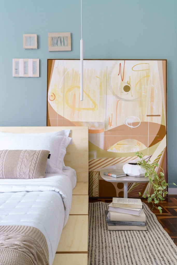 Projeto de Traama Arquitetura. Na foto, quarto com cama baixa, parede azul e quadro apoiado na parede.