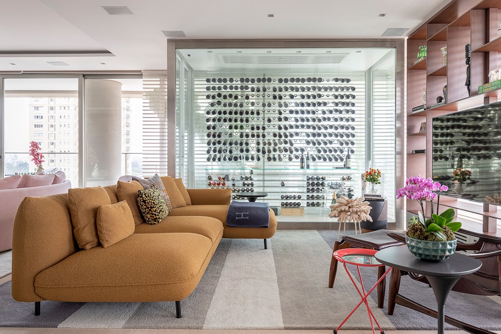 Apê descolado de 632 m² tem sofás coloridos e adega para mil garrafas. Projeto de Ana Weege. Na foto, sala de TV com adega e estante vazada.