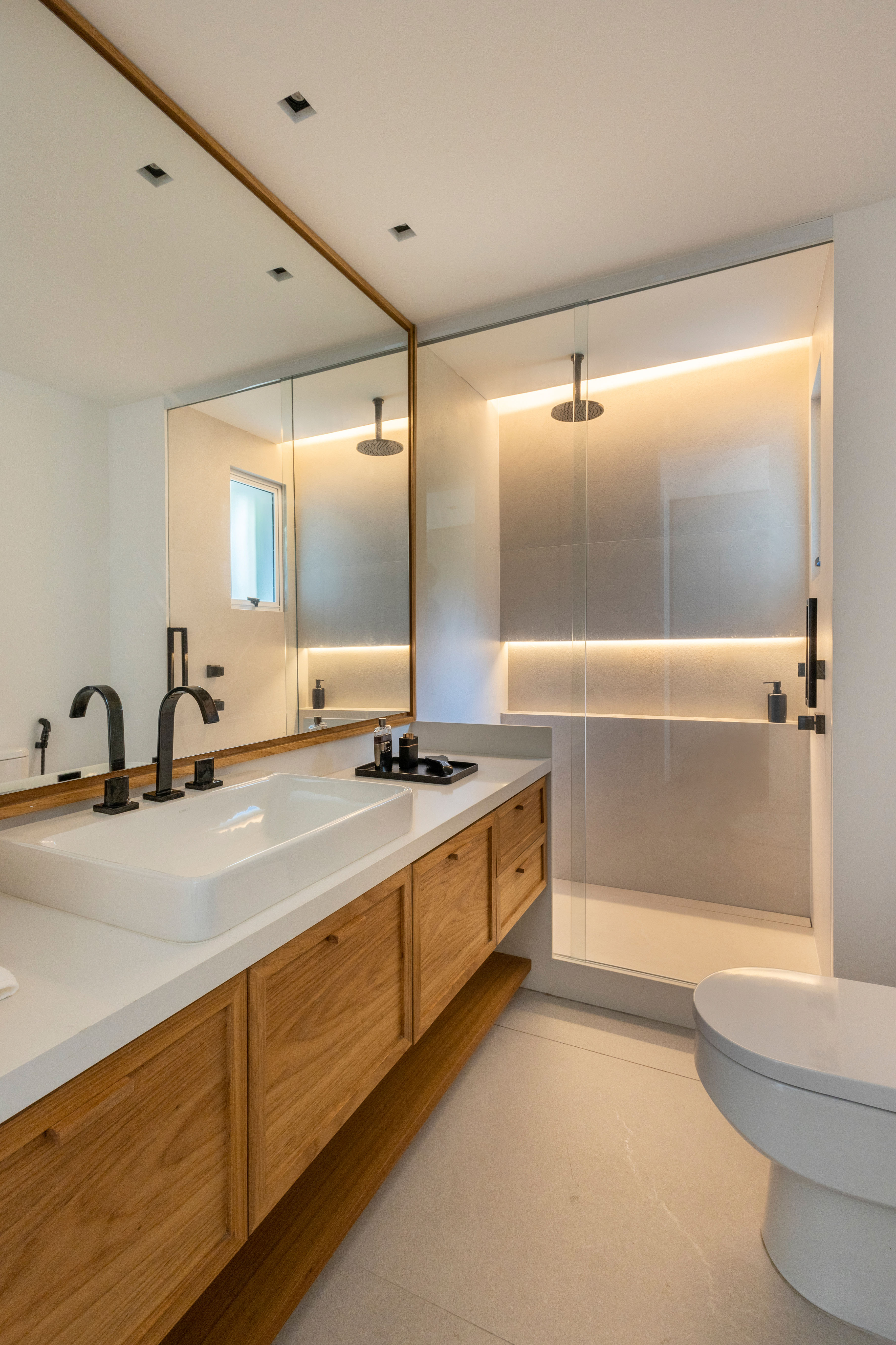 Projeto de Escala Arquitetura. Na foto, banheiro com bancada branca, box iluminado com nichos.