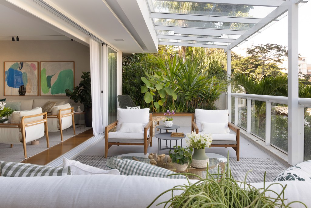 Projeto de Escala Arquitetura. Na foto, varanda com jardim integrado, sofá branco e poltronas brancas.
