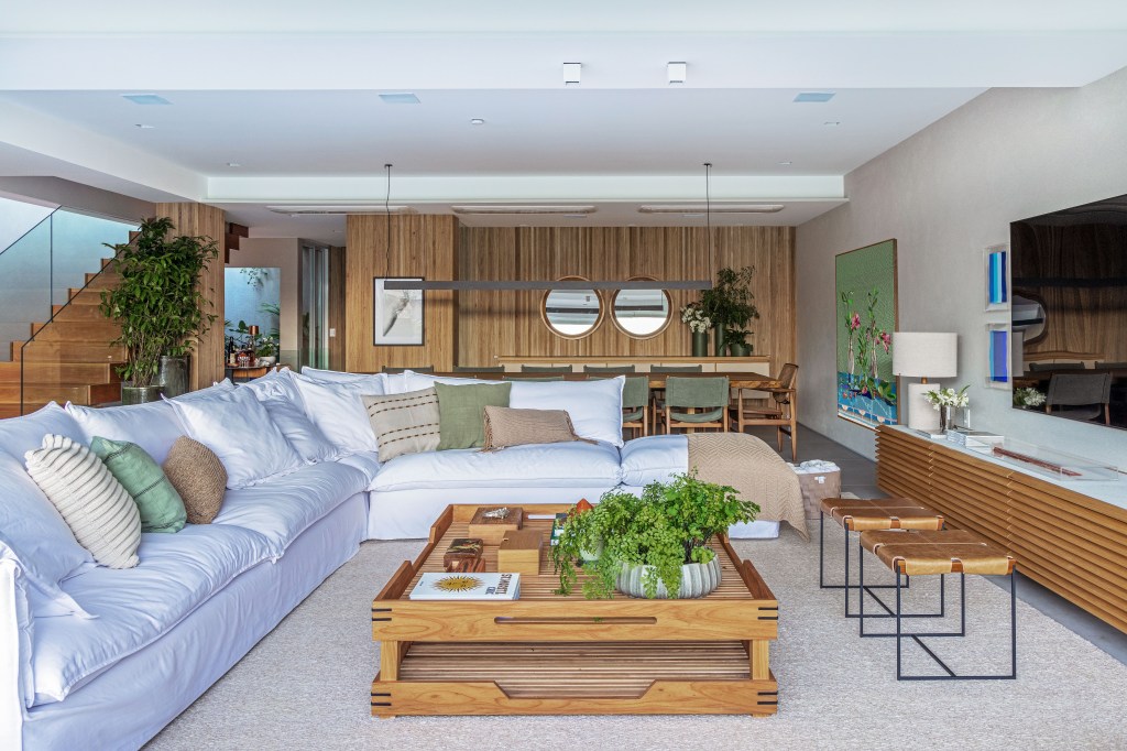 Projeto de Escala Arquitetura. Na foto, sala de estar com sofá branco com mesa de centro de madeira integrada com sala de jantar com parede revestida de madeira.