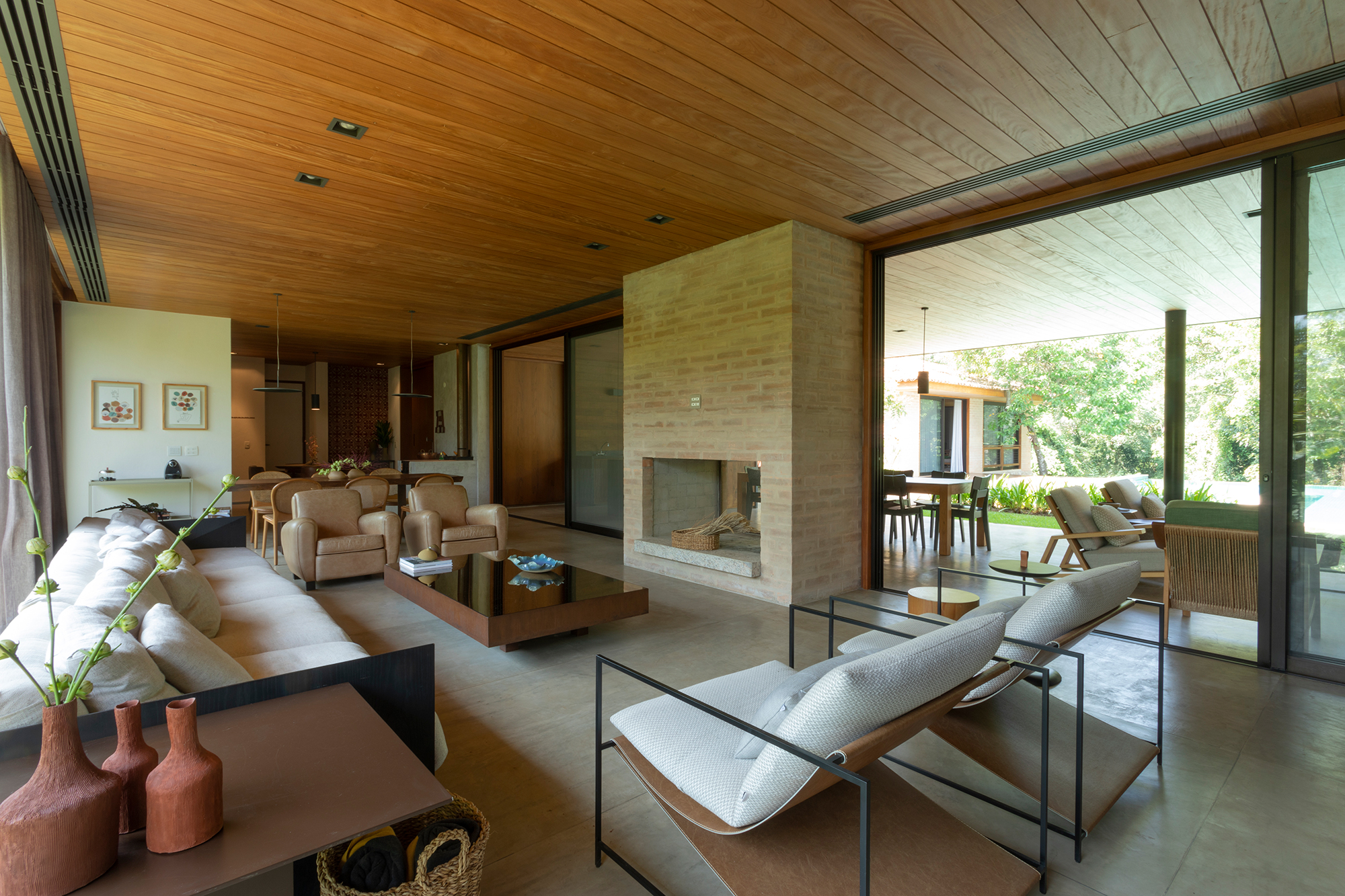 Casa de campo de 818 m² é um verdadeiro refúgio em meio à natureza. Projeto de Daniel Fromer. Na foto, varanda e sala com lareira, vista para o jardim e sofás.