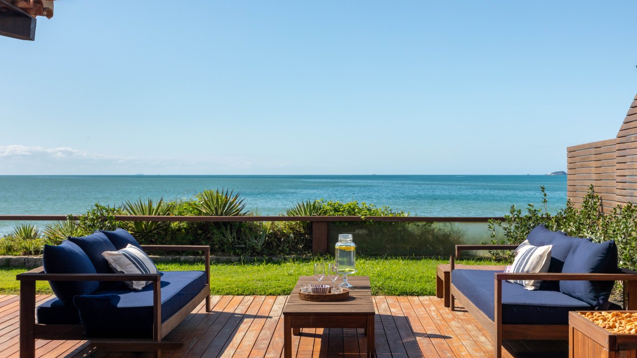 Projeto de Brise Arquitetura. Na foto, deck de madeira com sofás azuis e vista para o mar.