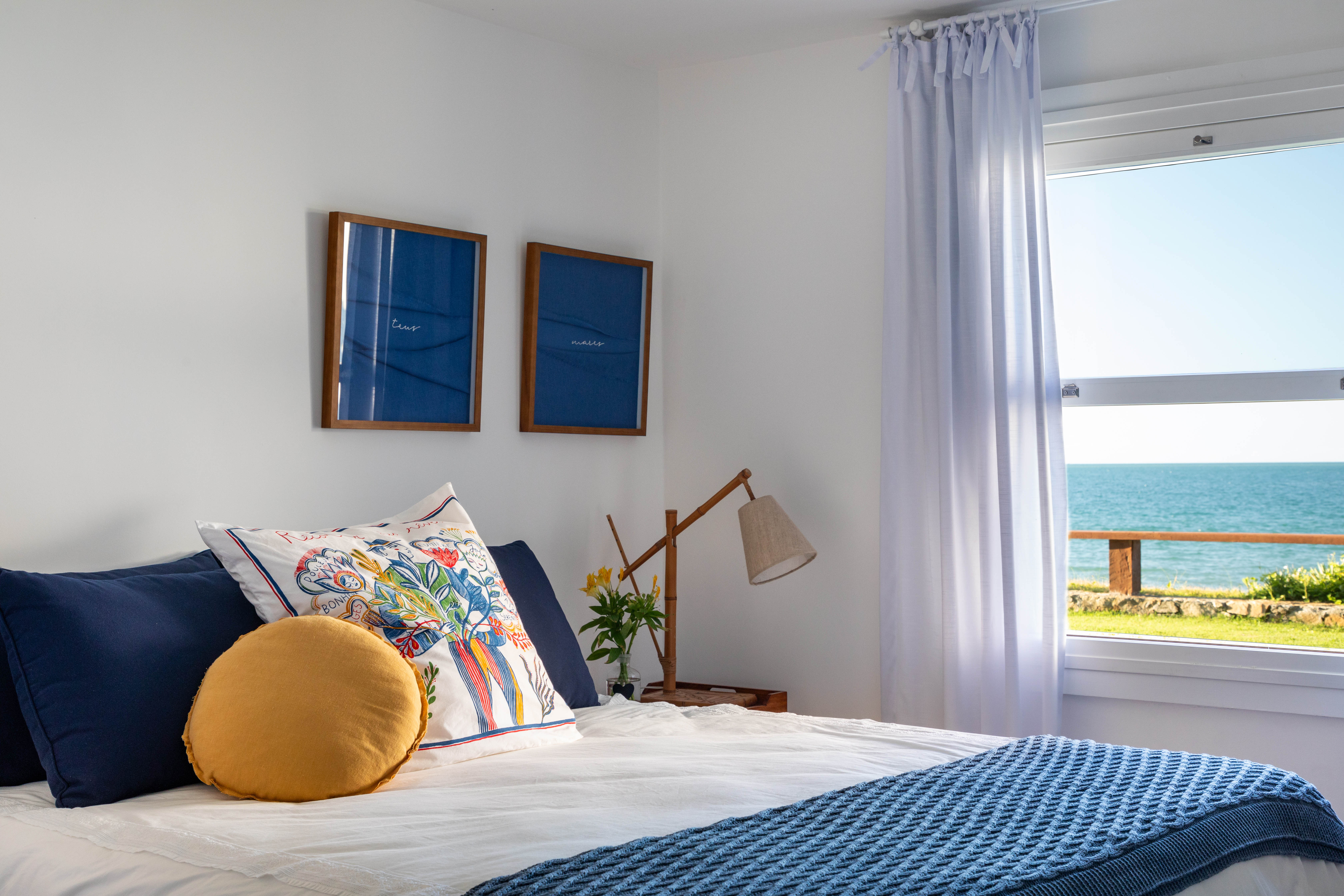 Projeto de Brise Arquitetura. Na foto, quarto com cama de casal, cortina branca e vista para praia.