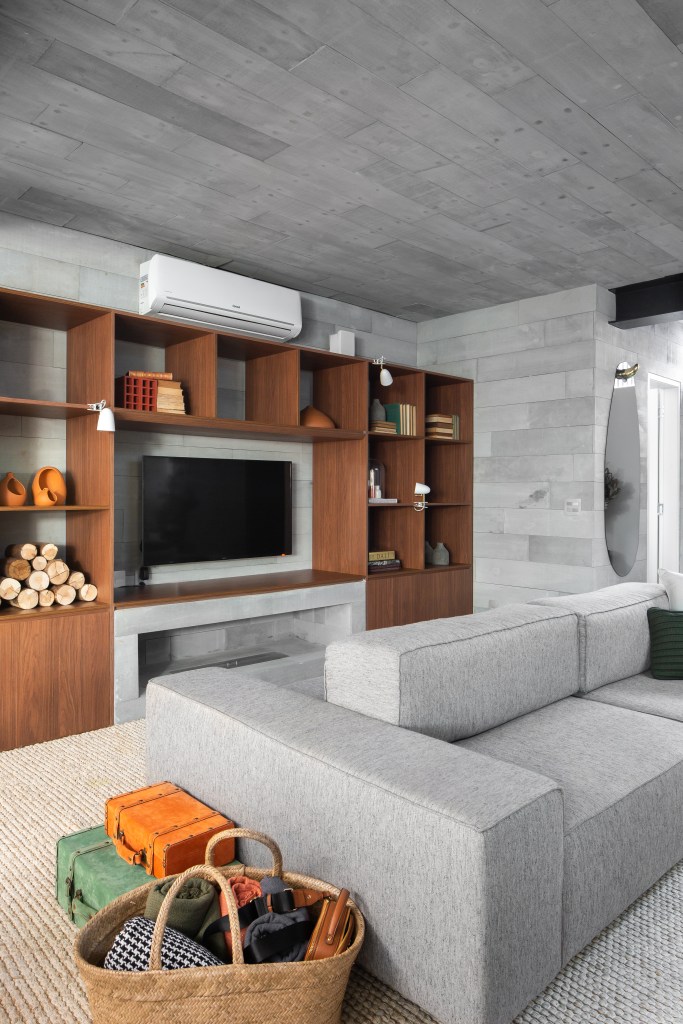 Projeto de M² Arquitetura. Na foto, sala com sofá ilha cinza e estante de marcenaria com nichos iluminados.