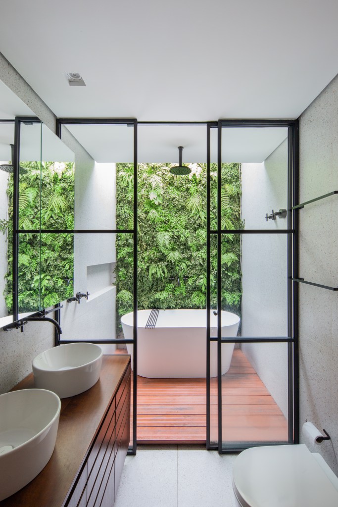 Projeto de M² Arquitetura. Na foto, banheiro com claraboia, banheira solta e jardim vertical.