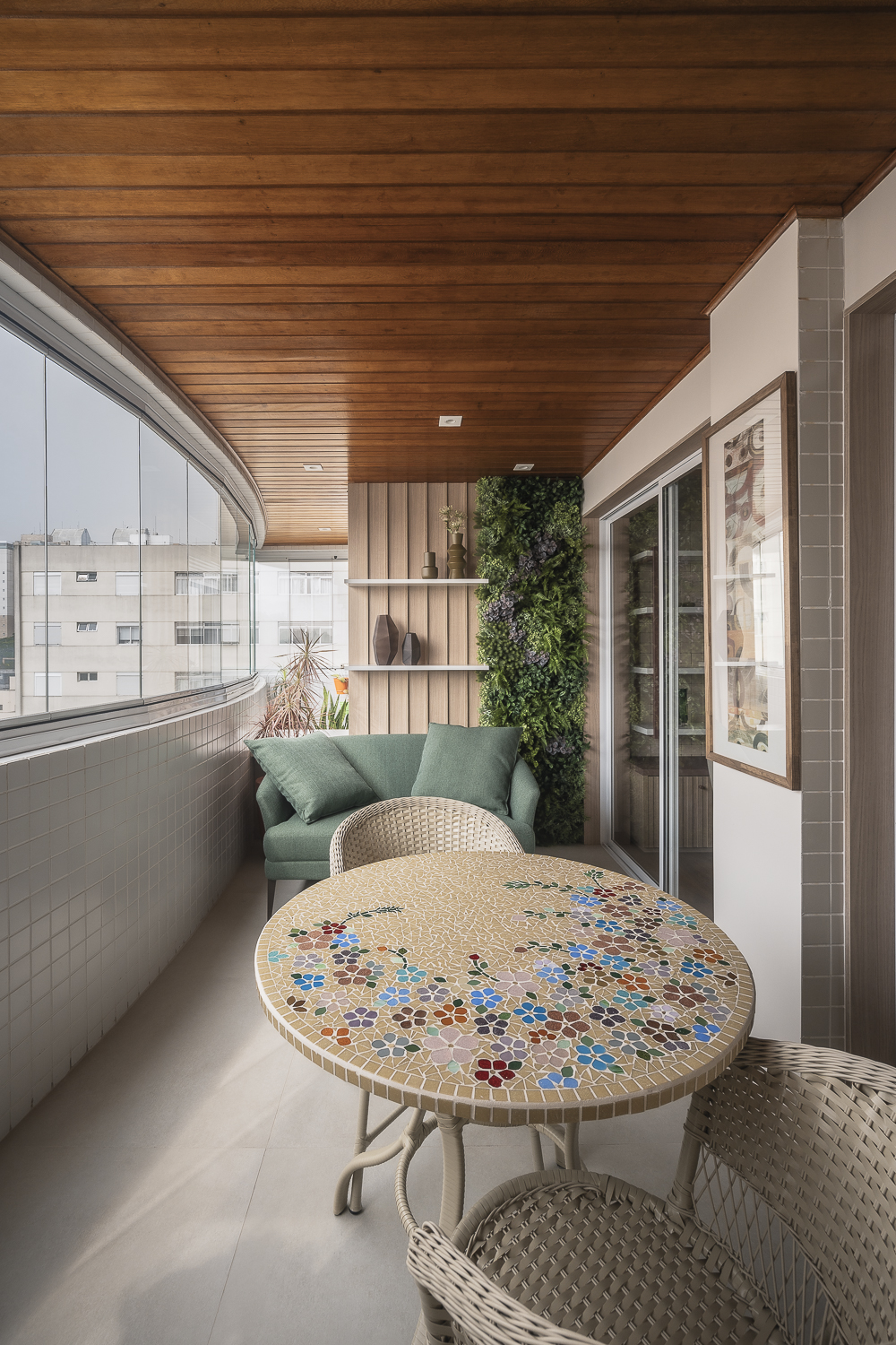 Projeto de Studio Ricciardi. Na foto, varanda com teto de madeira, sofá verde, mesa redonda pequena e marcenaria para plantas.