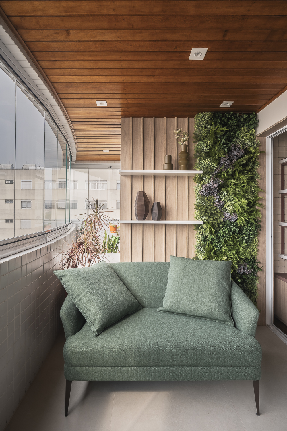 Projeto de Studio Ricciardi. Na foto, varanda com teto de madeira, sofá verde, mesa redonda pequena e marcenaria para plantas.