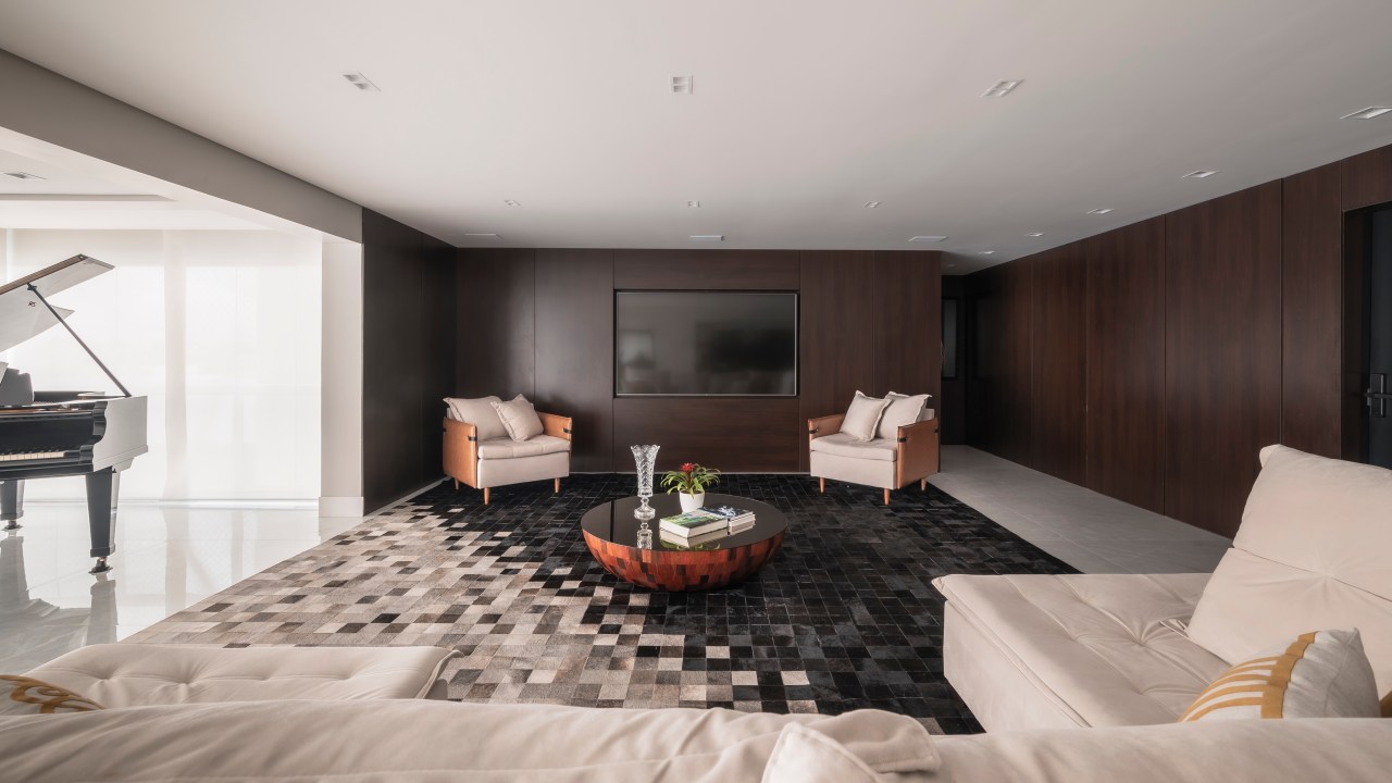 Projeto de PB Arquitetura. Na foto, sala de estar com parede revestida de madeira e tapete geométrico branco e preto.