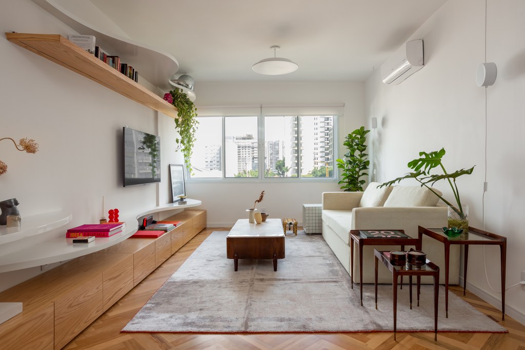 Concreto, verde e rosa marcam o décor deste apê de 110 m². Projeto de MNBR Arquitetos. Na foto, sala de estar com sofá cinza, mesa e tapete. Prateleira de TV curva.