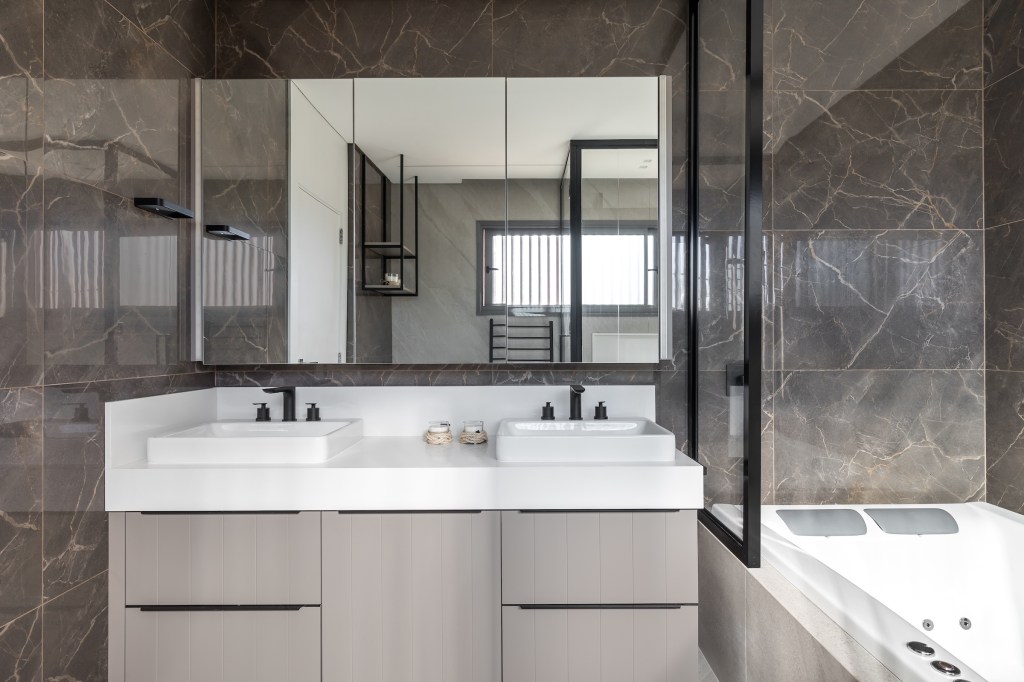 Projeto de Larissa Lóh. Na foto, banheiro com cuba dupla, banheira e revestimentos de porcelanato em padrão marmorizado.