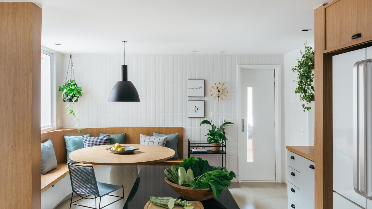 Projeto de Studio A+G Arquitetura. Na foto, cozinha clara com parede de azulejos, canto alemão e mesa redonda.