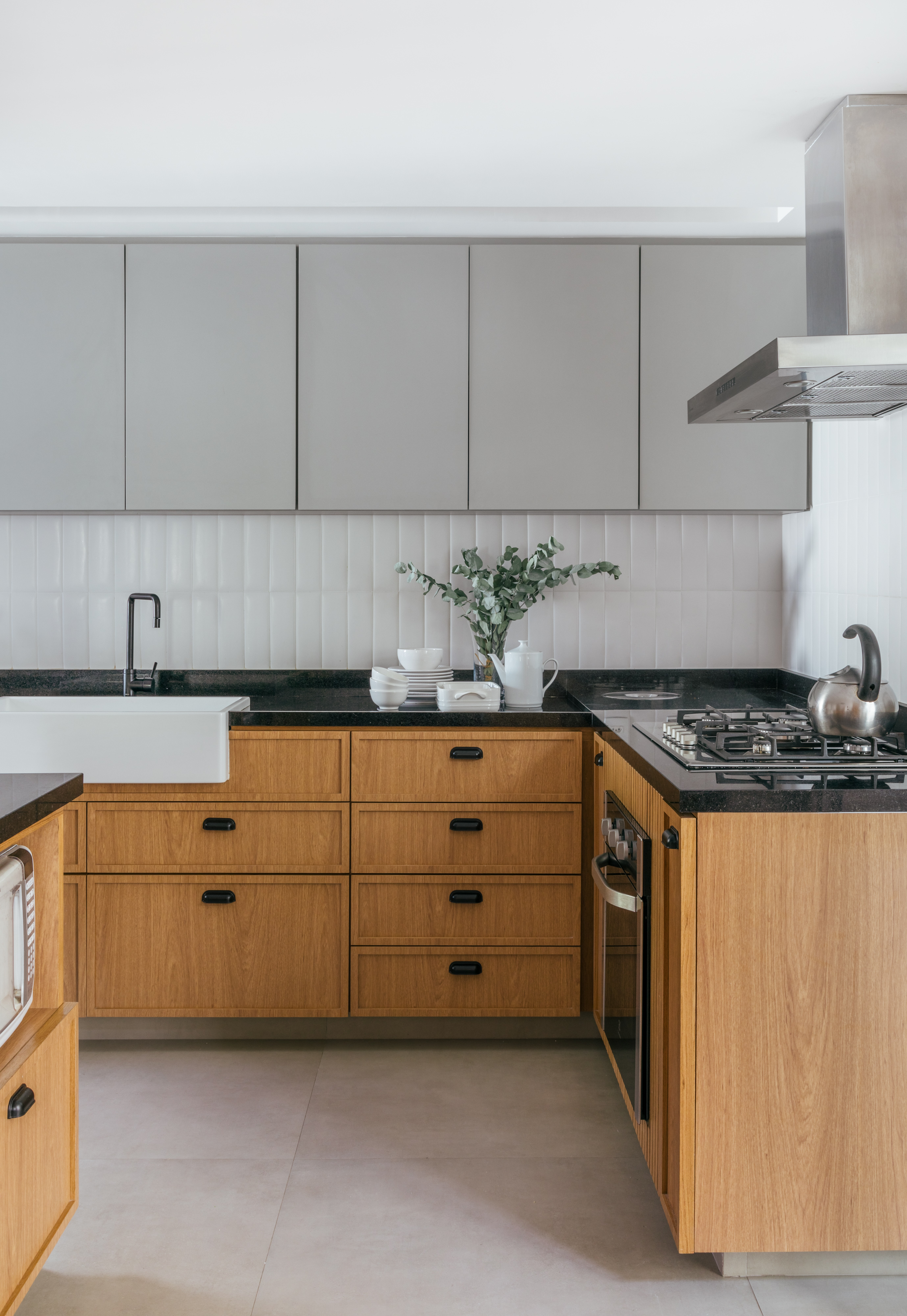Projeto de Studio A+G Arquitetura. Na foto, cozinha com armários cinza e amadeirados e bancada preta.