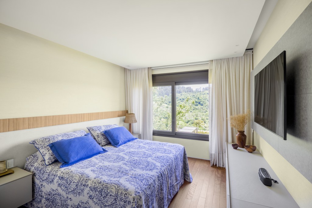 Projeto de TM Arquitetura. Na foto, quarto com cama de casal e janela com vista para paisagem.