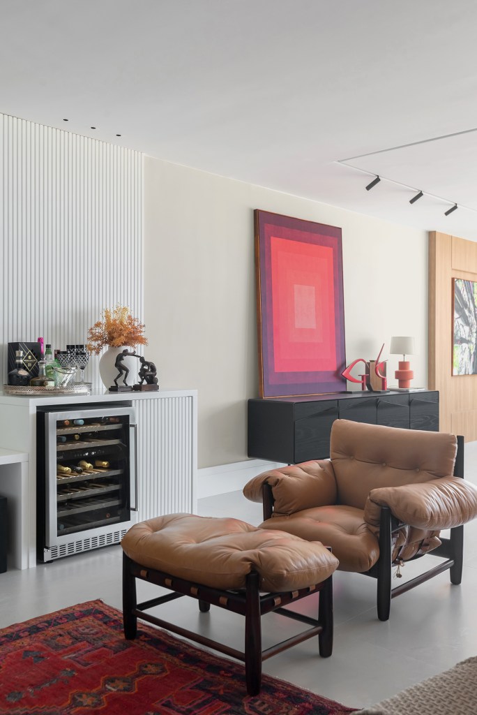 Dois apartamentos unidos criam casa de praia para a família em 370 m². Projeto de Maria Augusta Bittencourt, Na foto, aparador com quadro vermelho e poltrona mole.