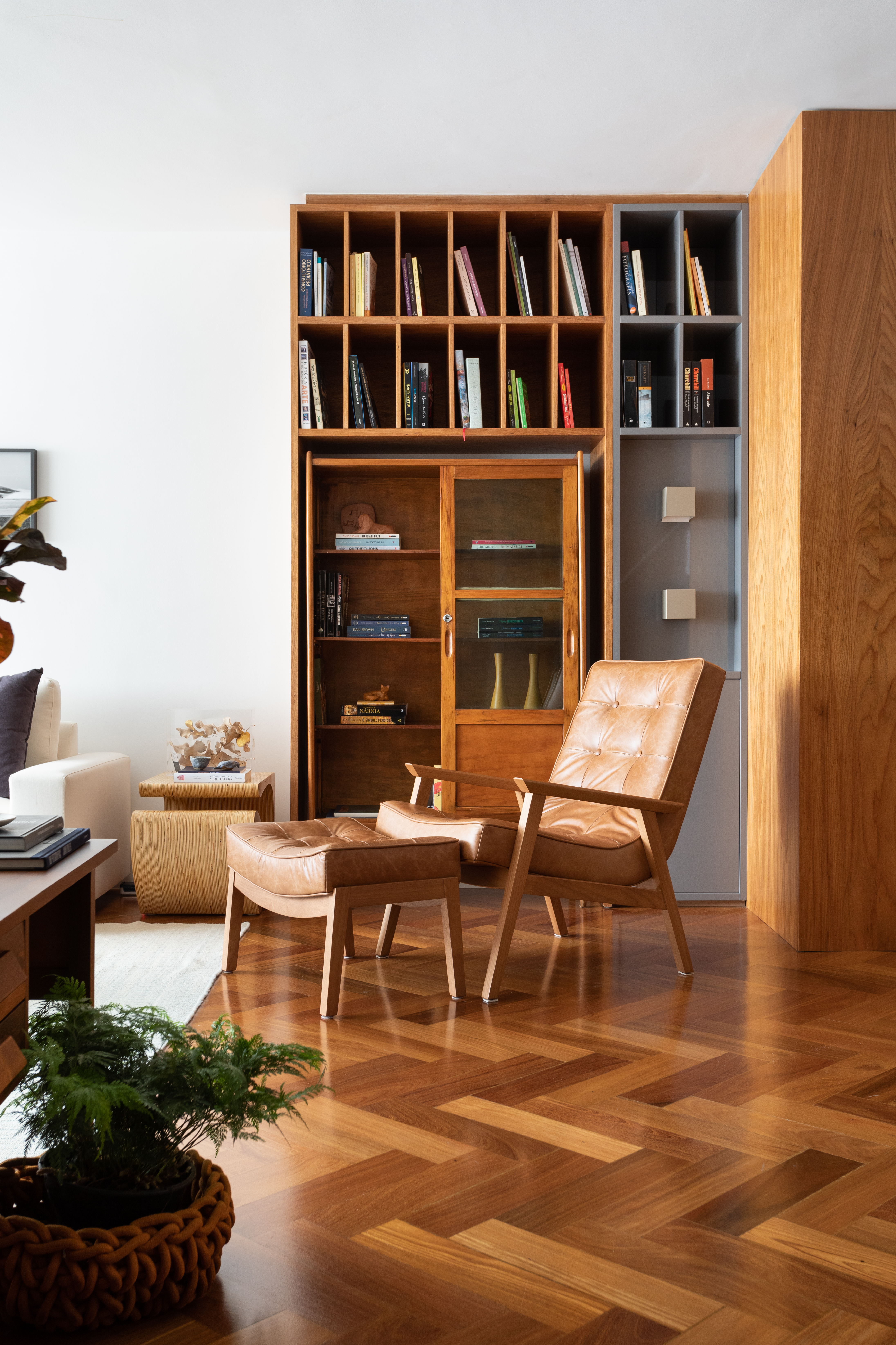 Projeto de Vivi Cirello. Na foto, sala com estante de madeira vintage e poltrona de couro marrom.