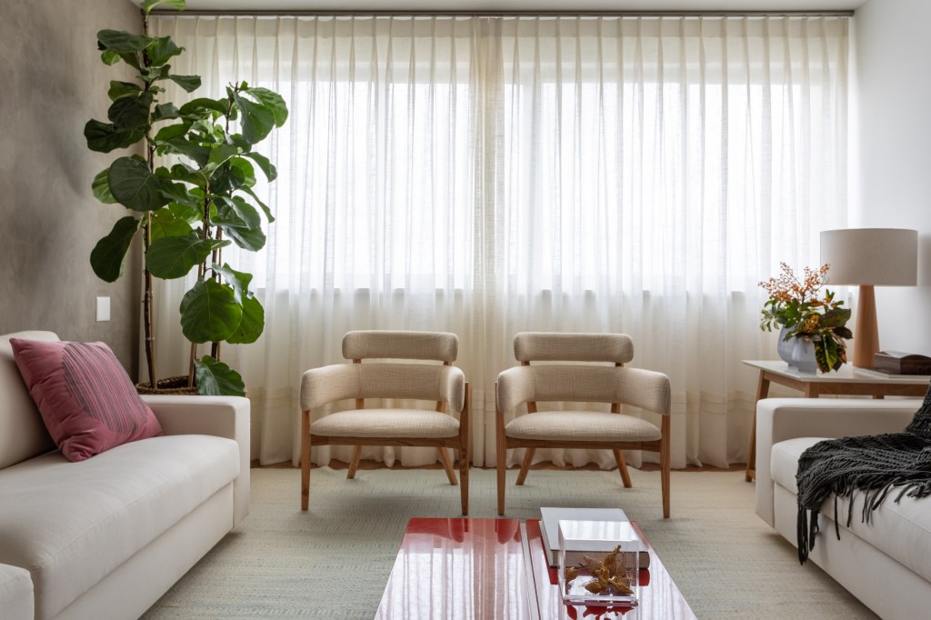 Projeto de Vivi Cirello. Na foto, sala de estar com tapete neutro, duas poltronas, planta ficus e cortina de linho.