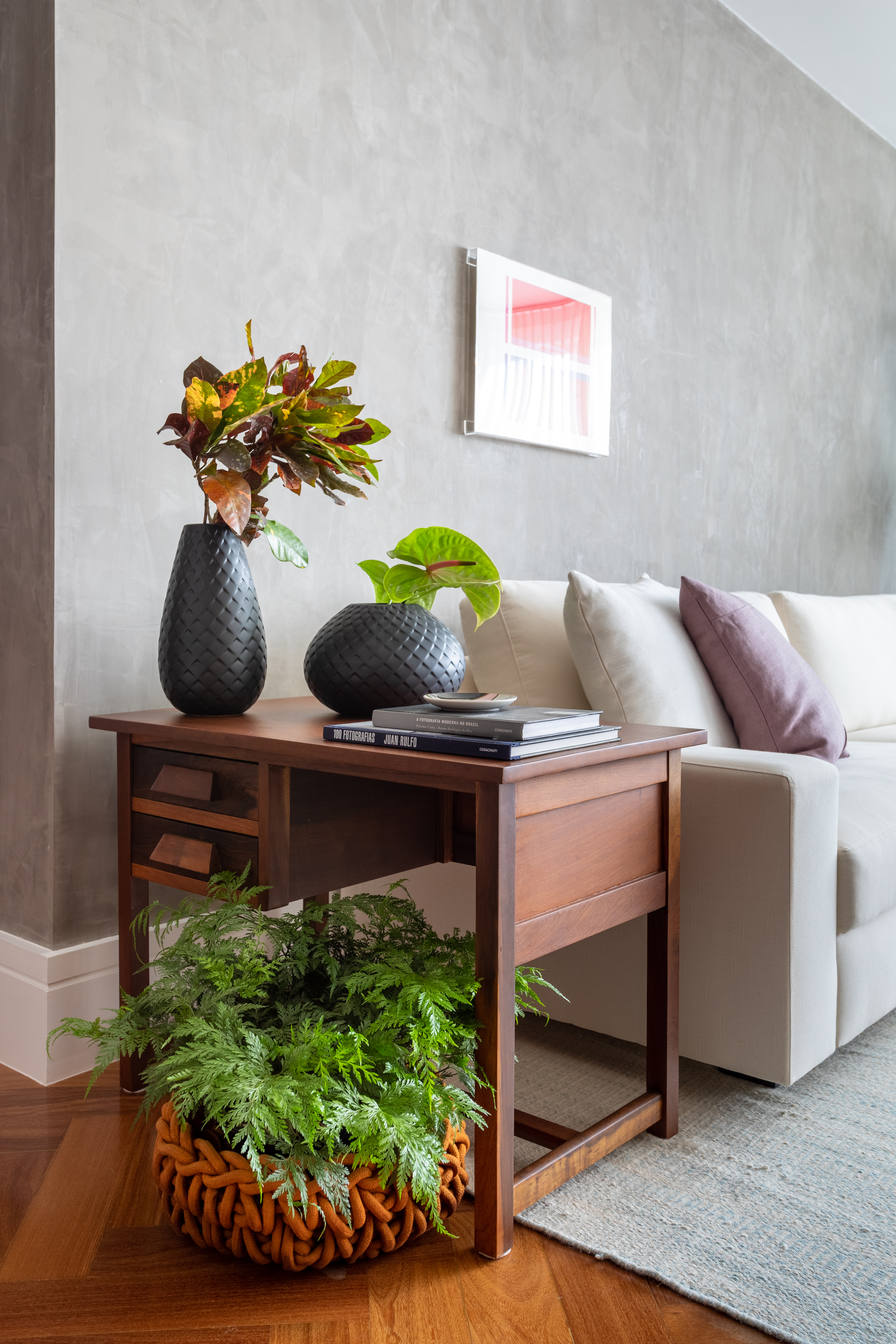 Projeto de Vivi Cirello. Na foto, sala com mesa lateral de madeira com plantas e sofá branco.