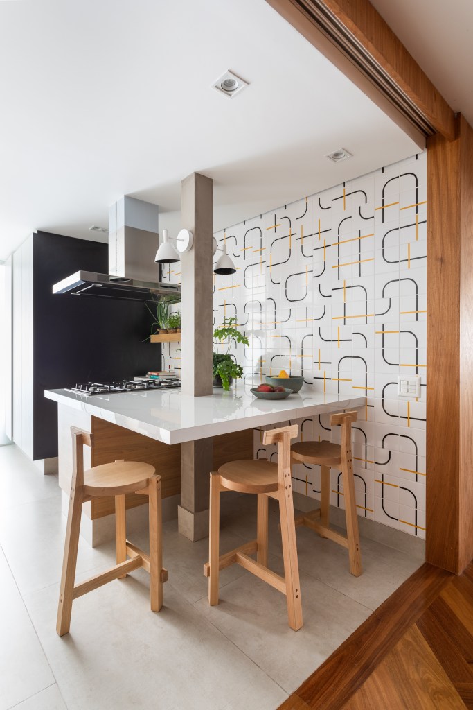Projeto de Vivi Cirello. Na foto, cozinha com ilha e bancada para refeições, parede de azulejos geométricos.