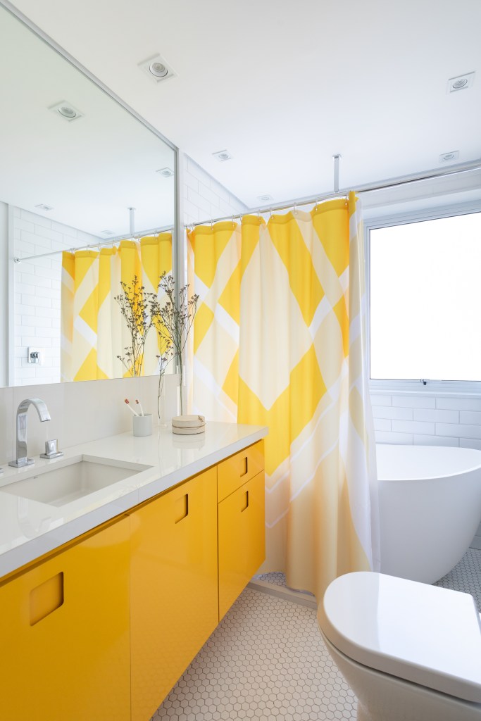 Projeto de Vivi Cirello. Na foto, banheiro com marcenaria amarela, banheira solta e cortina de banheiro amarela.