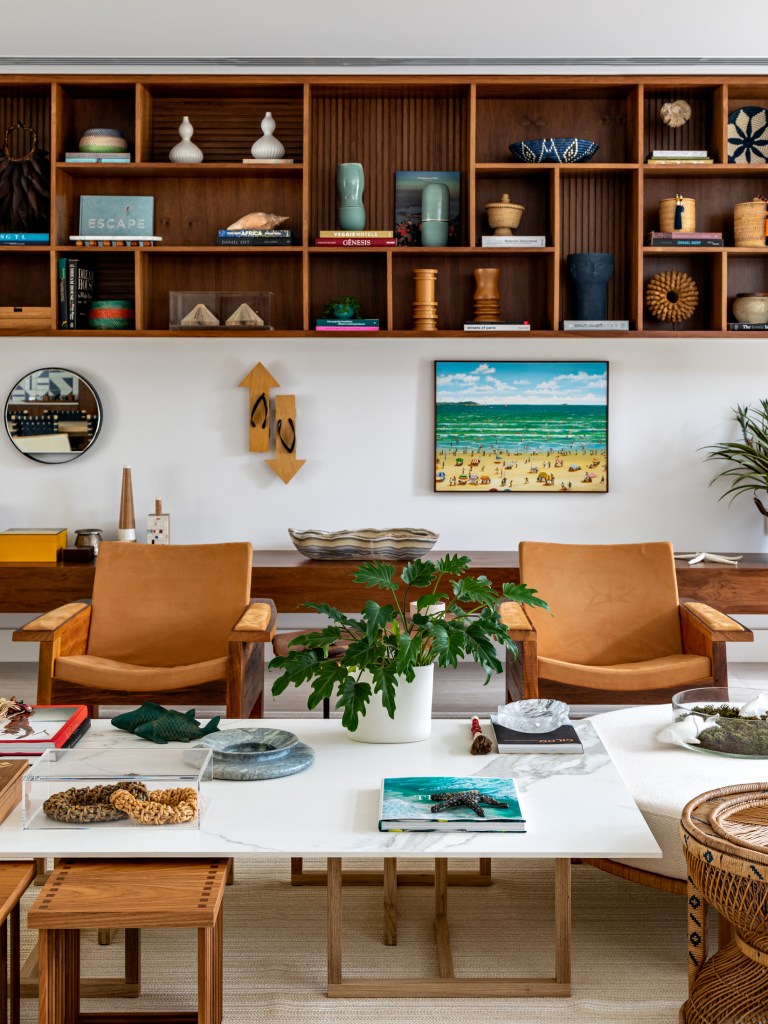 Grandes aberturas trazem a natureza para dentro desta casa de praia. Projeto de Marina Linhares. Na foto, sala de estar com poltronas de madeira e prateleira suspensa.