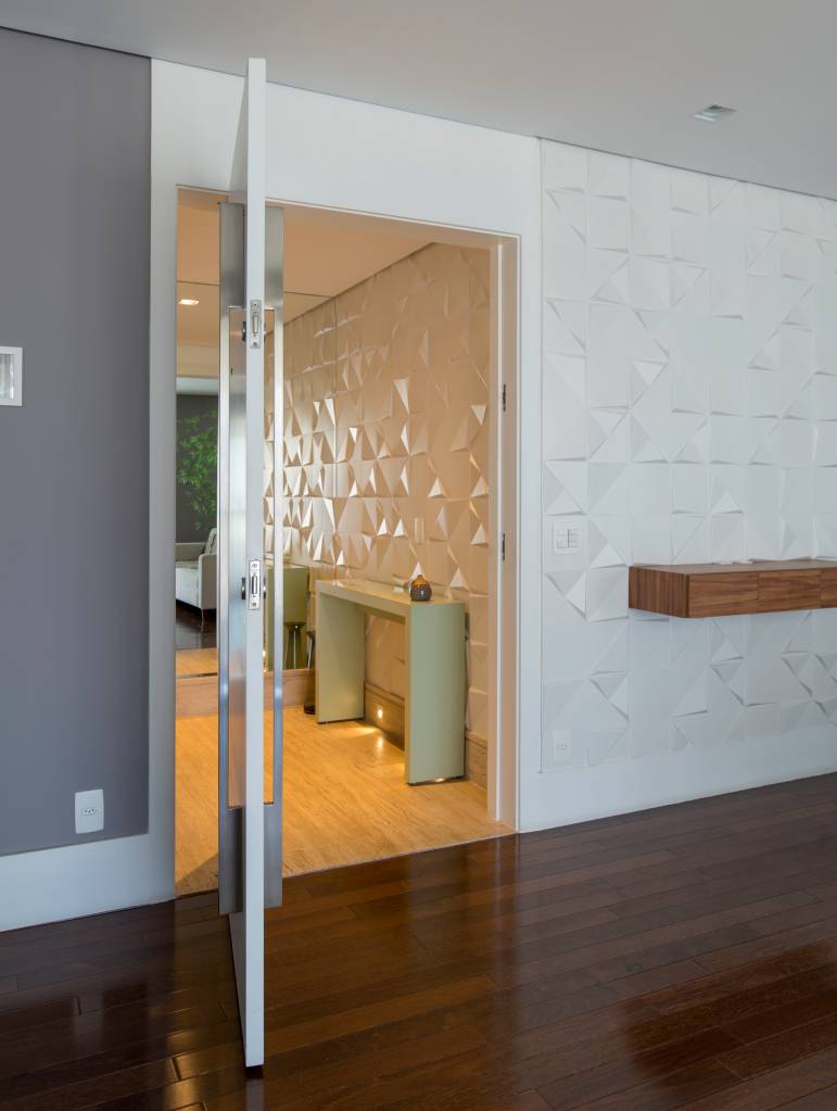Projeto de Raízes Arquitetos. Na foto, hall de entrada com revestimento 3d e porta pivotante.