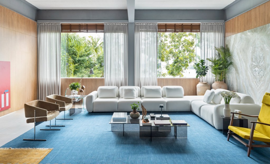 “Poetas do Futuro por Deca”, ambiente de Nathália Xavier para a CASACOR SC 2023. Na foto, living com tapete azul, sofá branco e mesa de centro.