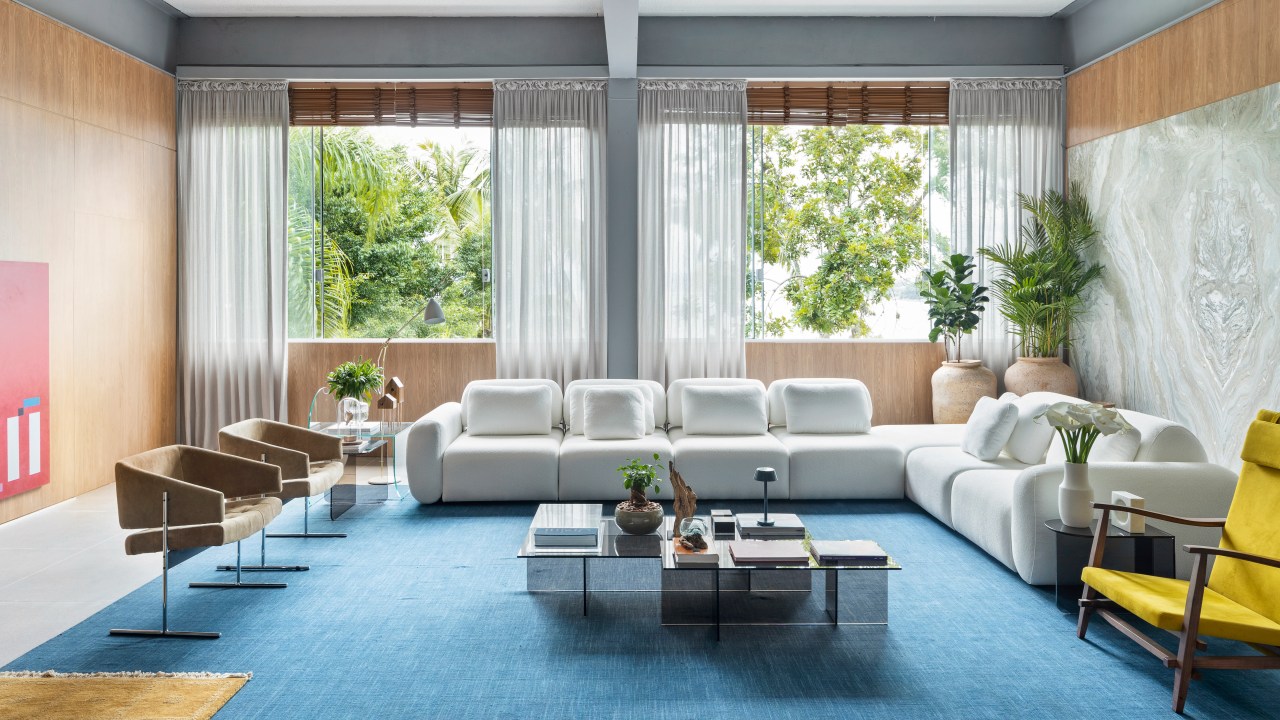 “Poetas do Futuro por Deca”, ambiente de Nathália Xavier para a CASACOR SC 2023. Na foto, living com tapete azul, sofá branco e mesa de centro.