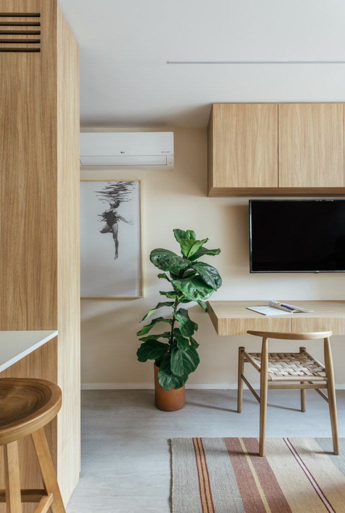 Projeto de Rodolfo Consoli. Na foto, sala com bancada de madeira, armário de madeira e planta ficus.