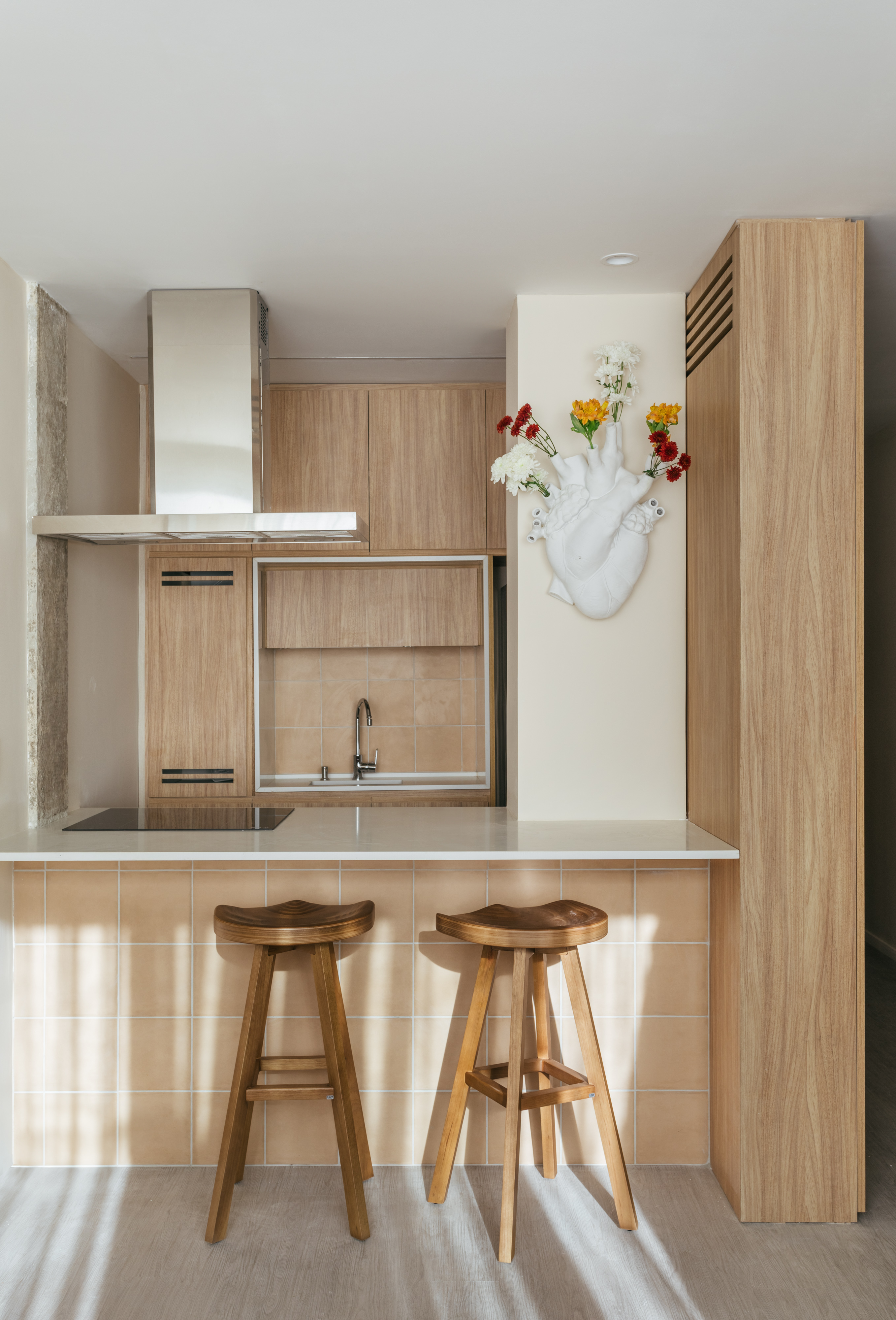 Projeto de Rodolfo Consoli. Na foto, cozinha integrada pequena com marcenaria clara e banquetas de madeira.